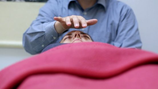 Healer der holder hånd over ansigtet på en kvinde der ligger under et rødt tæppe